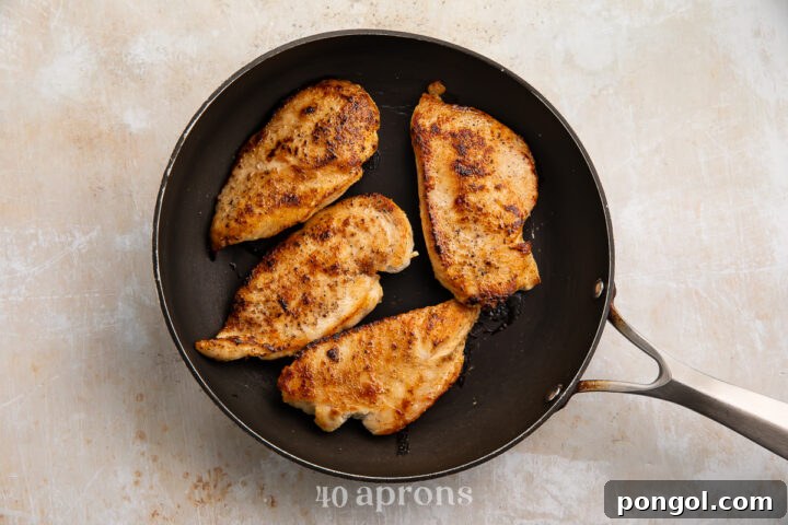 Overhead view of 4 chicken cutlets in a large cast iron skillet. Cutlets have been fried until golden brown.