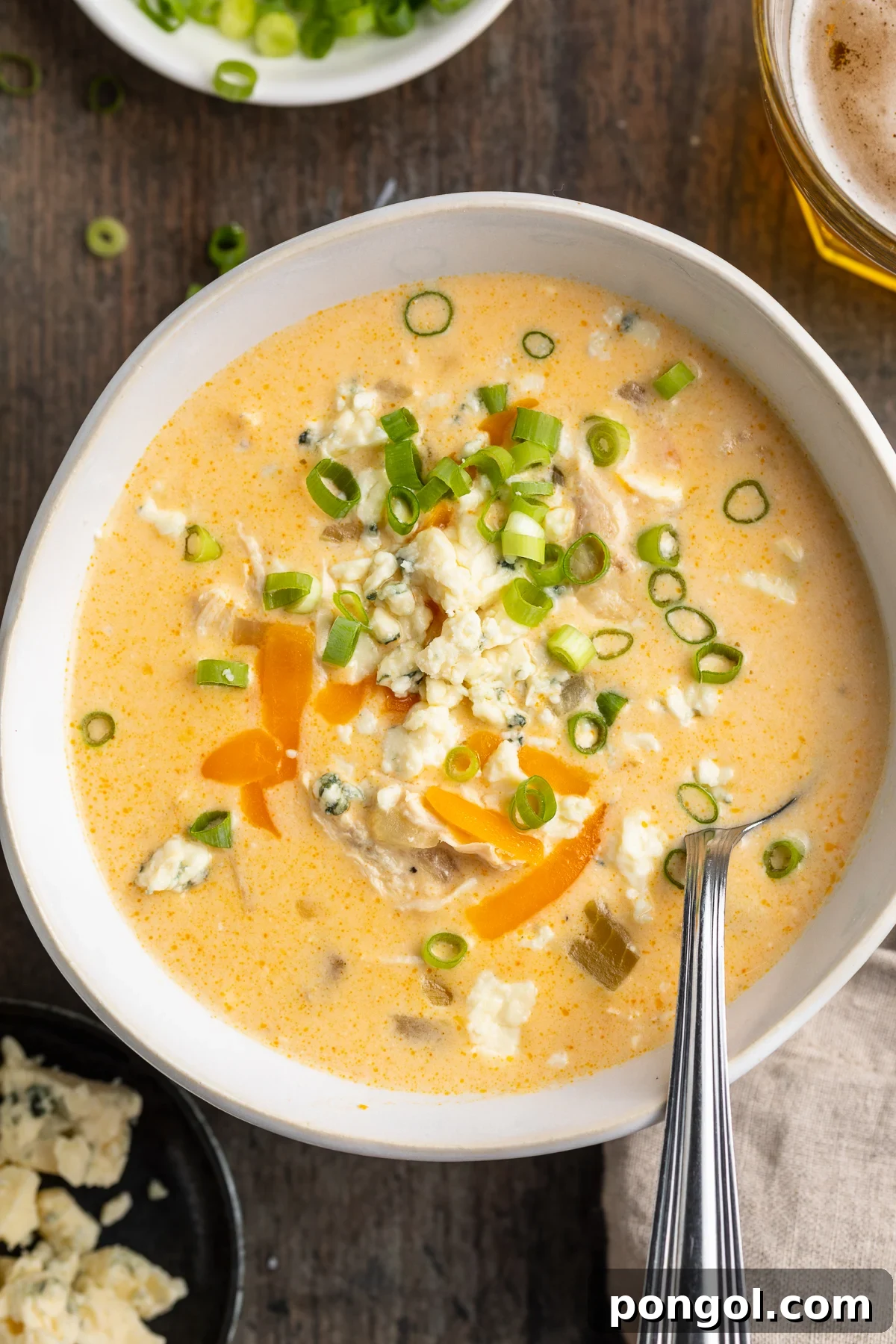 Overhead view of a steaming bowl of creamy buffalo chicken soup, garnished with fresh herbs, on a rustic wooden table.