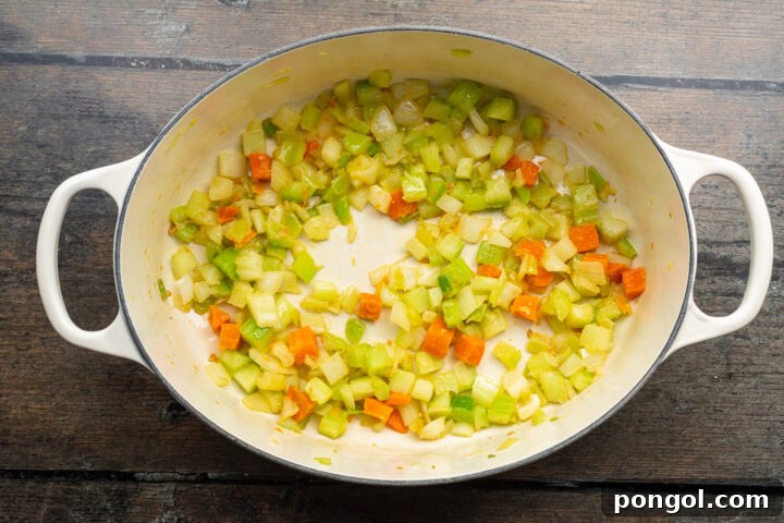 Overhead view of a large soup pot with butter, onion, celery, carrots, and garlic sautéing on a wooden table.