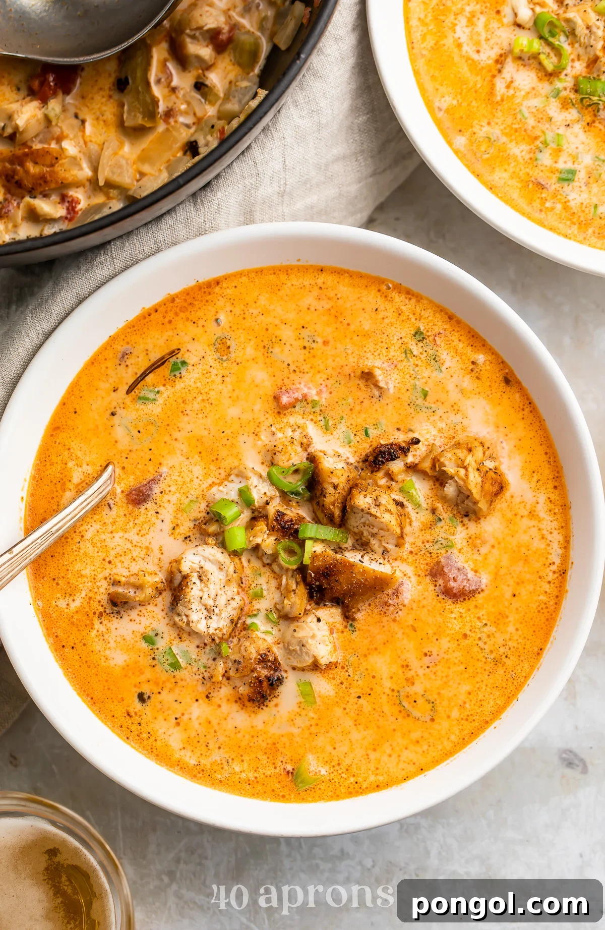 Overhead, zoomed-in view of a bowl of creamy cajun chicken soup in a white soup bowl with a silver spoon on a marble countertop.