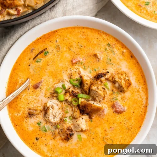 Overhead, zoomed-in view of a bowl of creamy cajun chicken soup in a white soup bowl with a silver spoon on a marble countertop.