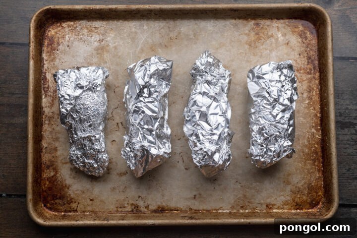 Effortless Holiday Feast 5 Foil-wrapped sweet potatoes baking on a sheet pan