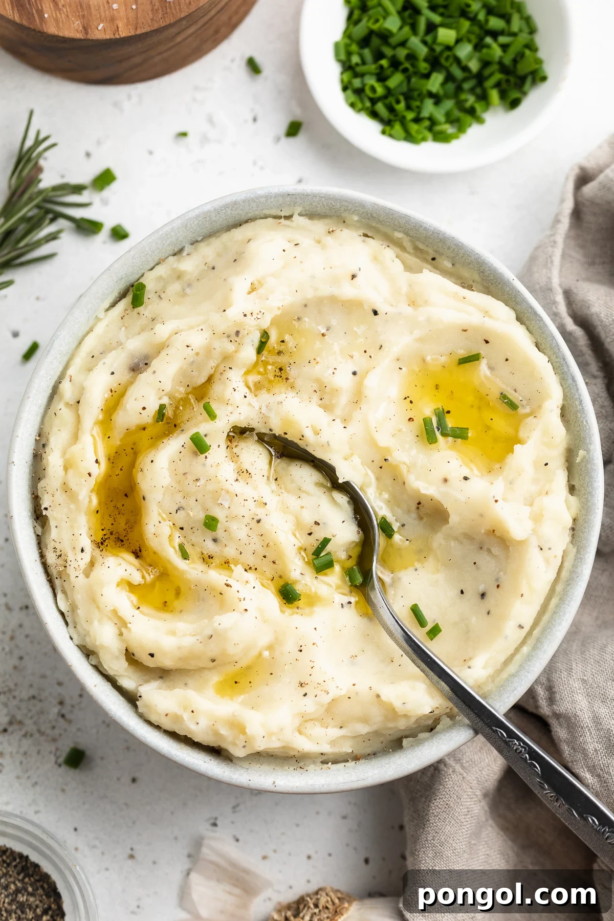 Velvety Vegan Mashed Potatoes 2 Overhead view of a bowl of dairy-free mashed potatoes on a white table top. A silver spoon rests in the potatoes.