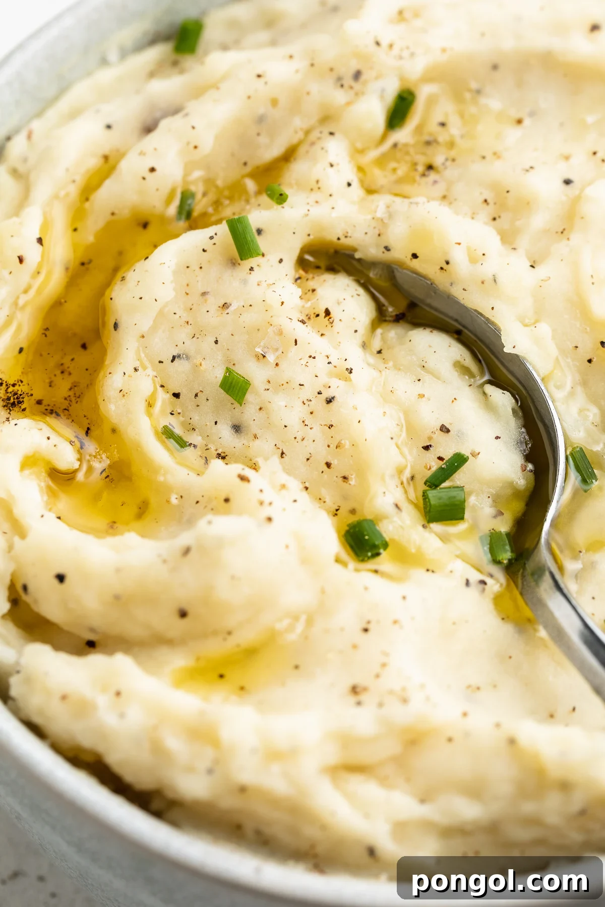 Velvety Vegan Mashed Potatoes 3 Close-up, overhead view of the left half of a large white bowl holding dairy-free mashed potatoes topped with brown gravy.