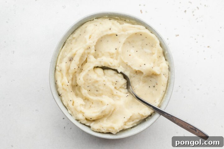 Velvety Vegan Mashed Potatoes 7 Overhead view of creamy dairy-free mashed potatoes in a large white bowl with a silver spoon.