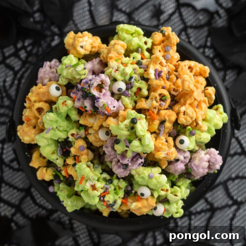 Overhead view of a plastic cauldron filled with orange, purple, and green white chocolate covered popcorn clusters with sprinkles and candy eyes.