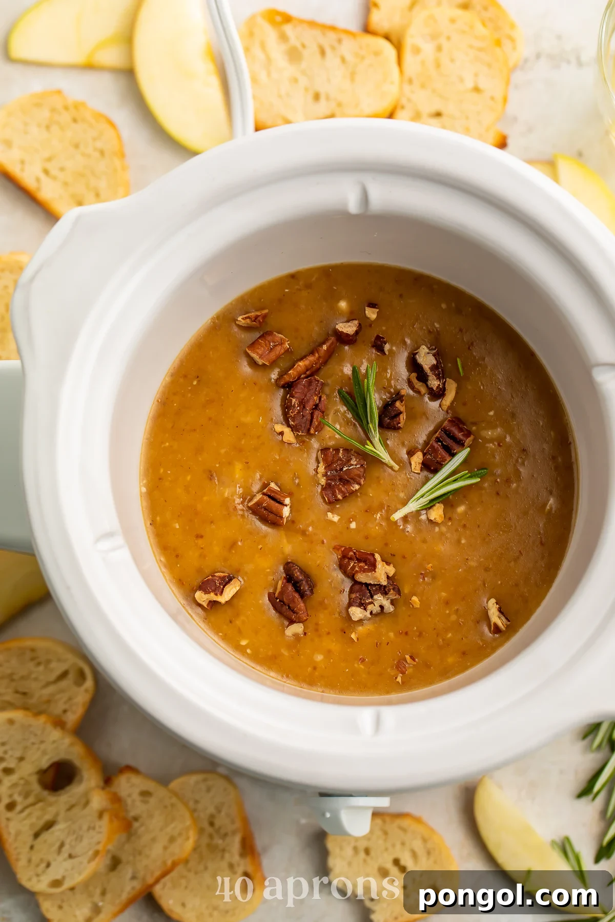 Overhead view of a small Crockpot containing a deep orange brie dip topped with freshly chopped pecans, ready for serving.