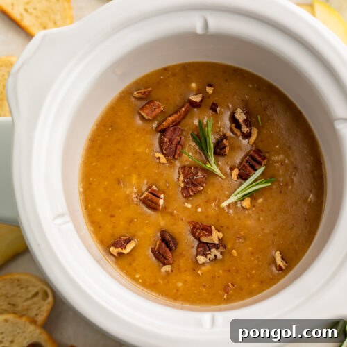 Overhead view of a small Crockpot containing a deep orange brie dip topped with chopped pecans.