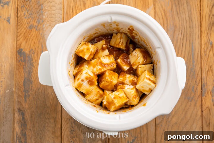 Overhead view of cubed brie cheese in a small white Crockpot with apricot preserves and apple juice.
