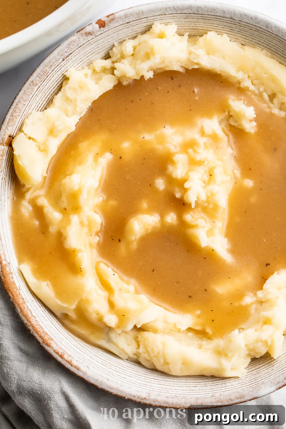 An overhead view of a bowl of fluffy mashed potatoes topped with a beautifully golden gluten-free gravy.
