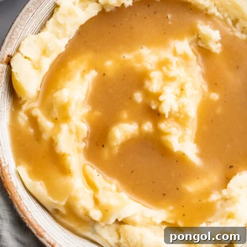 An overhead view of a bowl of fluffy mashed potatoes topped with a beautifully golden gluten-free gravy.