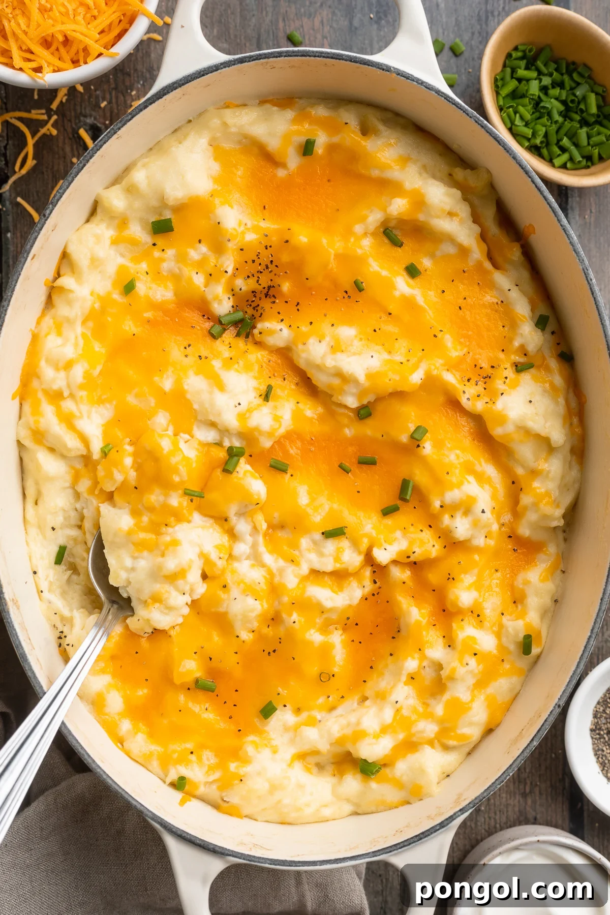 Overhead view of a large oval dish holding fluffy, creamy, cheesy mashed potatoes topped with cheddar cheese.