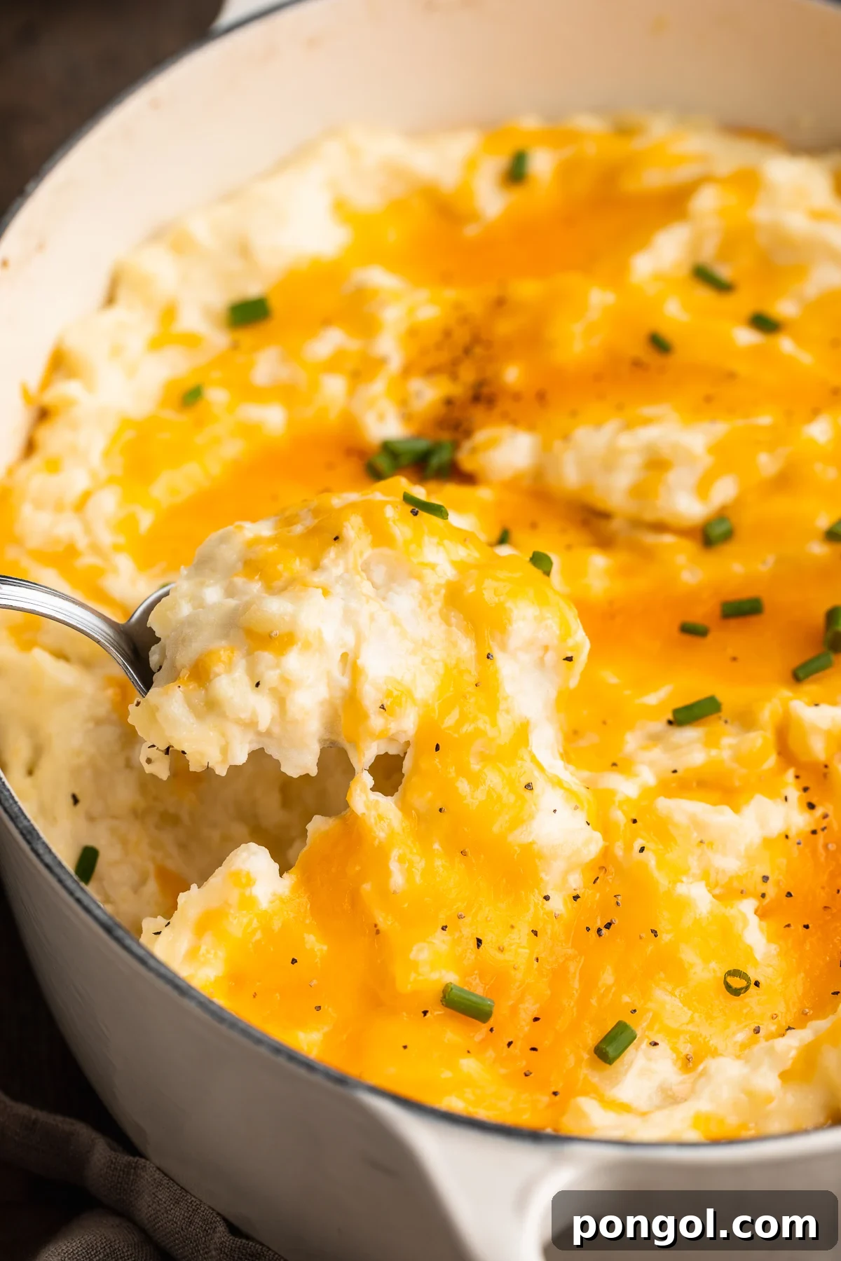 Side view of a scoop of cheesy mashed potatoes being lifted out of a large casserole dish with a spoon.