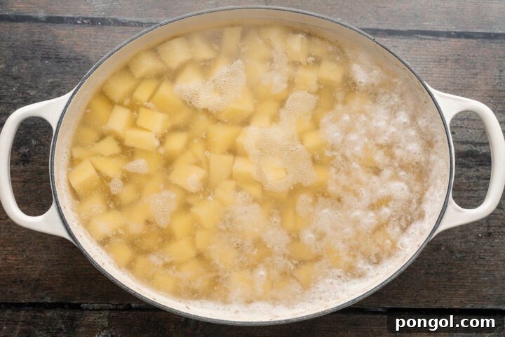 Overhead view of cubed potatoes in salted boiling water in a handled baking dish.