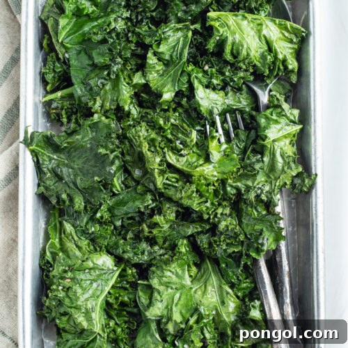 Overhead view of a large sheet pan holding leaves of bright green roasted kale on a neutral tablecloth.