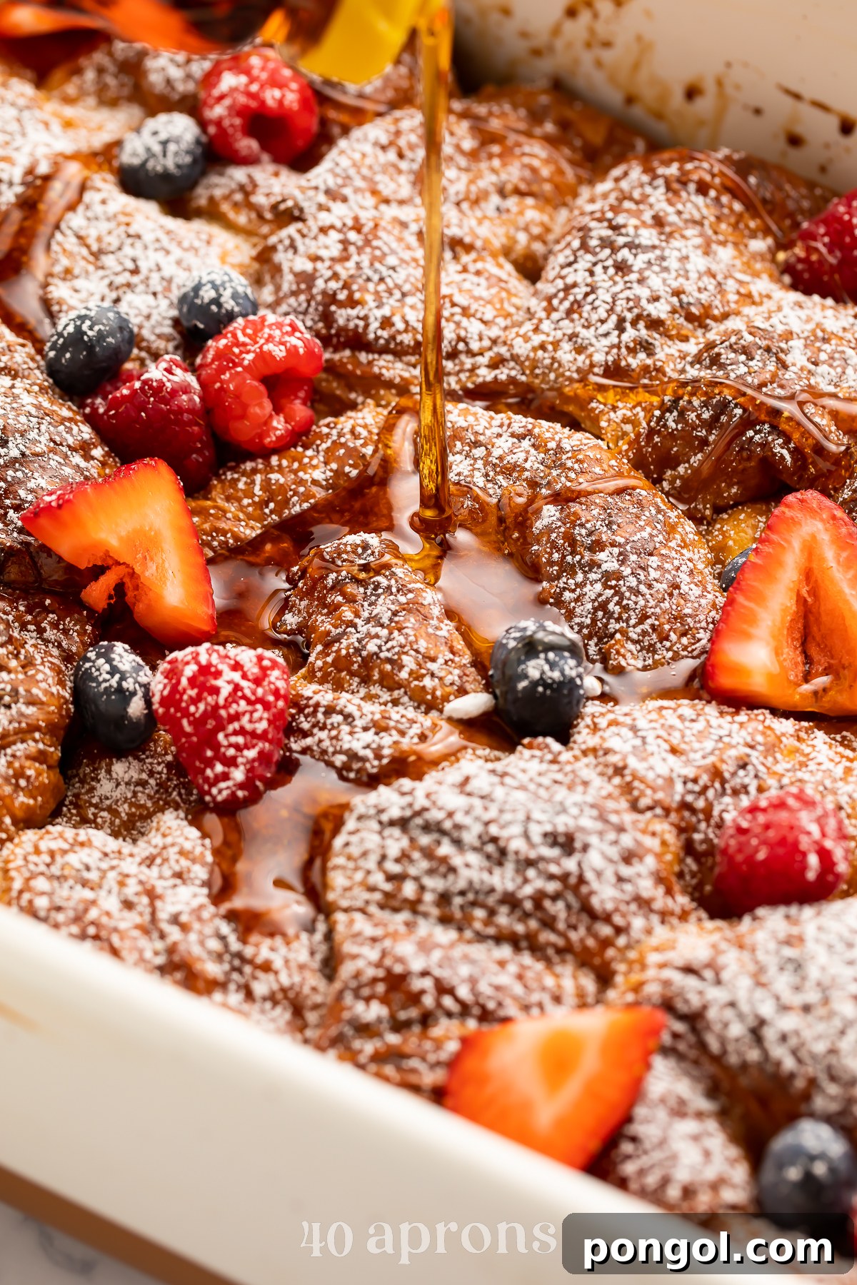 Close-up look at a croissant french toast casserole with brown sugar cinnamon in a casserole dish with strawberries and blueberries.