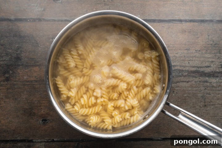Overhead view of rotini pasta boiling in a large silver pot of water.