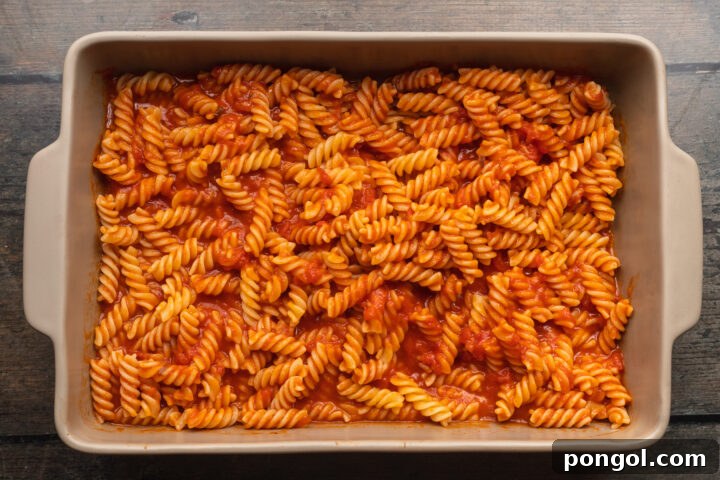 Overhead view of pasta and marinara sauce in a large rectangular baking dish.