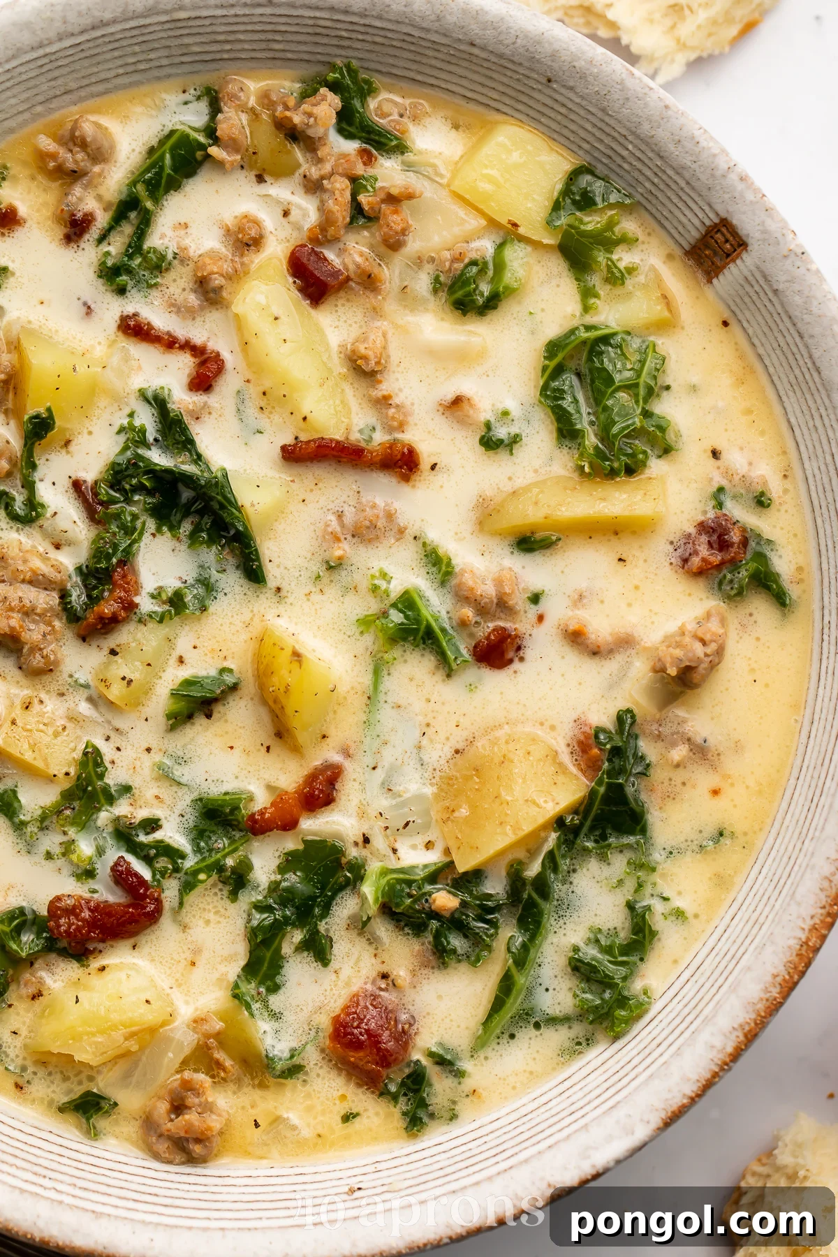 Close-up, overhead view of the right half of a bowl of zuppa toscana with kale, bacon, potatoes, and sausage.