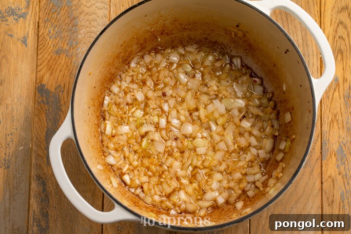 Overhead view of sautéed, translucent onions and minced garlic in rendered bacon fat in a large dutch oven.