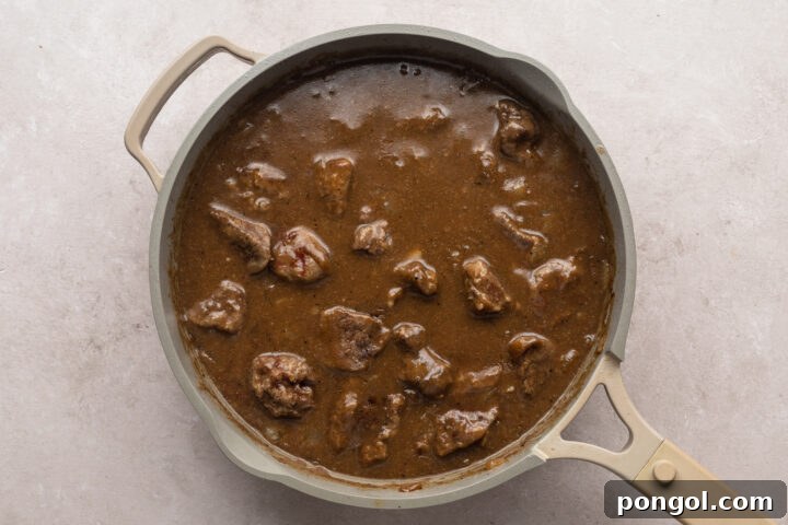 Overhead view of cooked beef tips in a pool of dark brown gravy in a large skillet.
