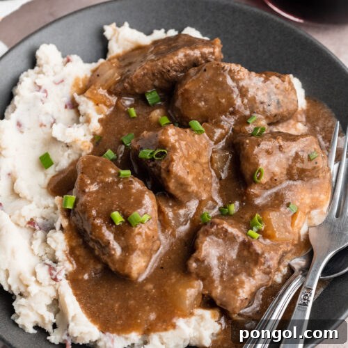 Overhead view of beef tips and gravy plated with white rice on a dark shallow bowl.