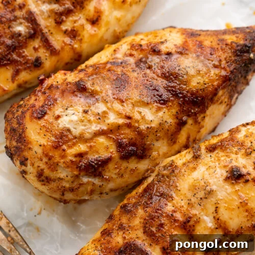 Overhead view of seasoned air fryer chicken breasts cooked from frozen lined up diagonally across a cutting board.