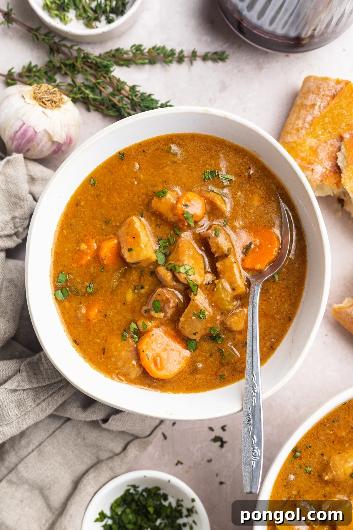 Overhead view of a bowl of pork stew on a table with recipe ingredients scattered around.