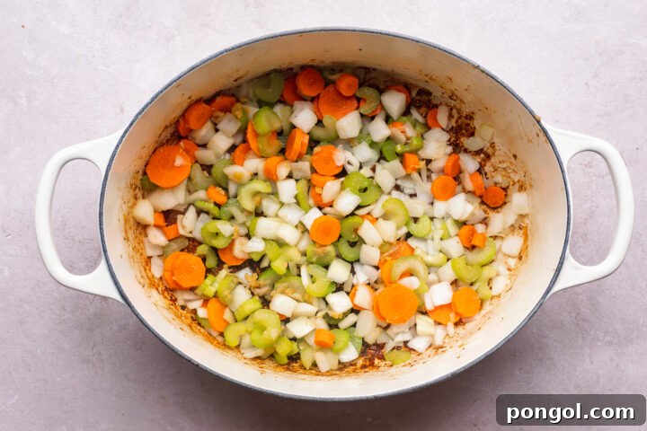 Overhead view of pork, carrots, onions, celery in a large dutch oven.