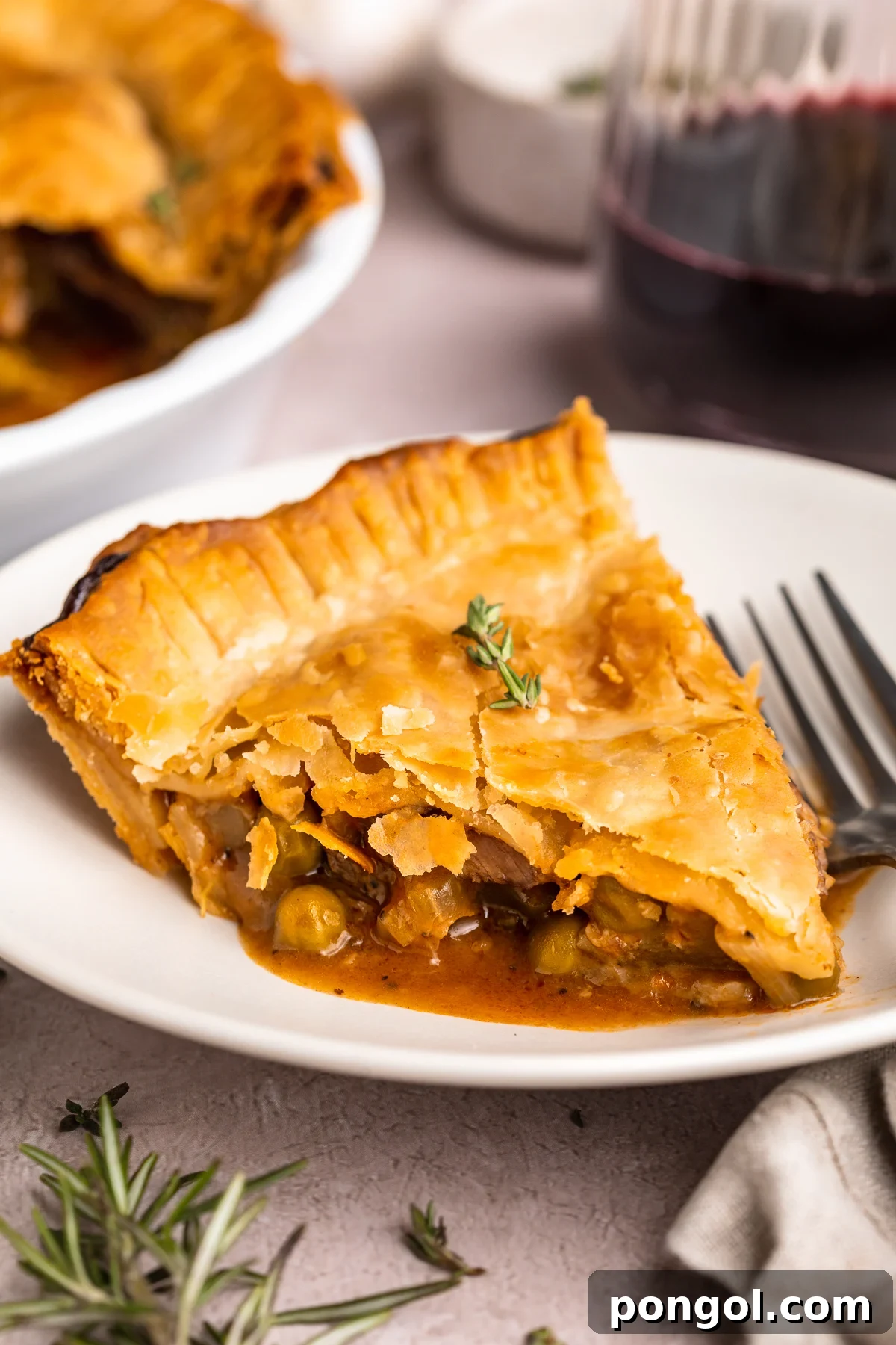 A wedge-shaped slice of beef pot pie on a white plate with a silver fork. The edge of the remaining pot pie is in the background.