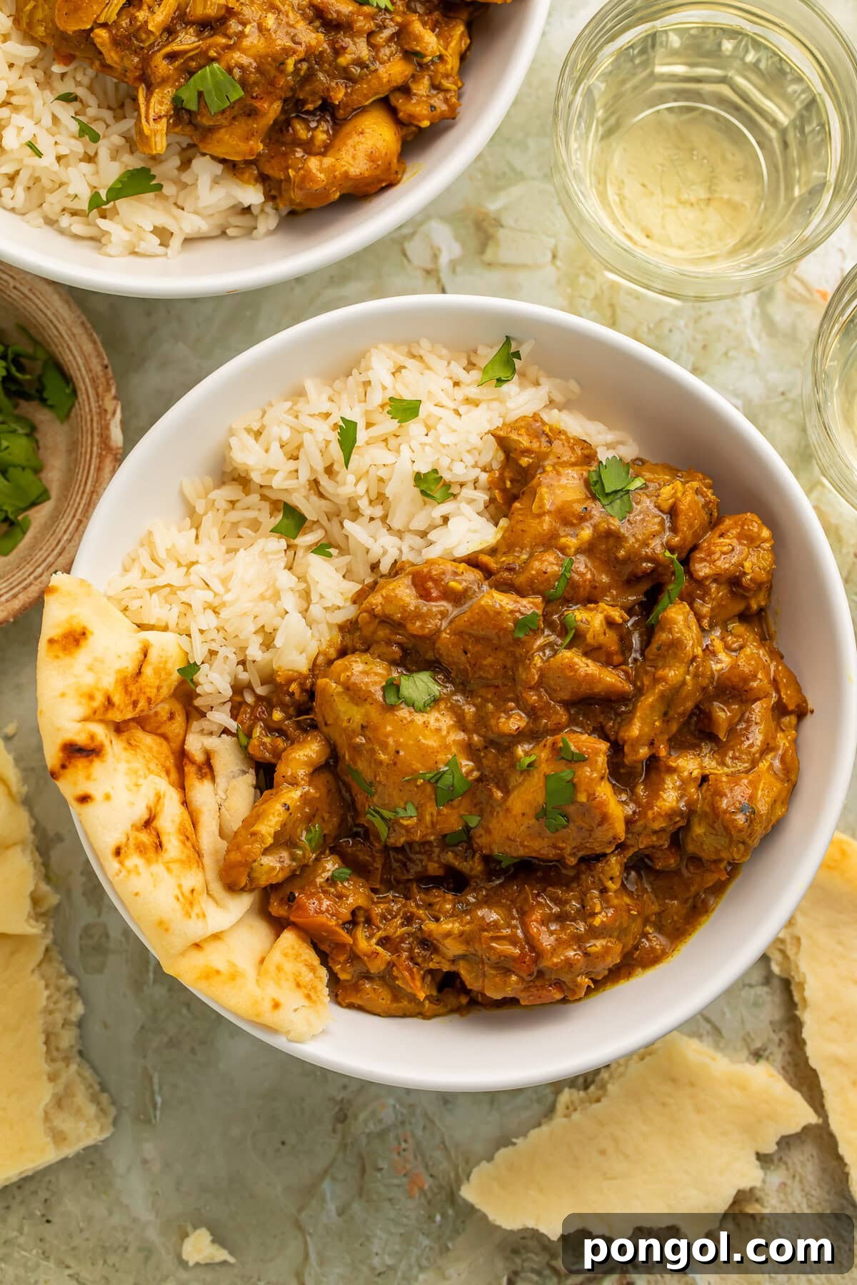Restaurant-style chicken curry served over basmati rice with naan in a white bowl
