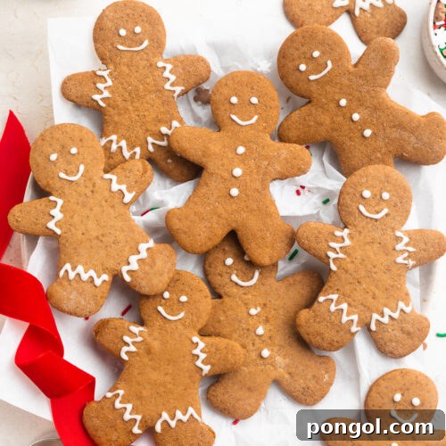 Overhead photo of gluten-free gingerbread men decorated with white cookie icing on a white table with red ribbon and holiday sprinkles.