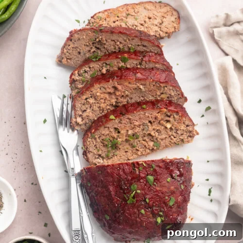 A Whole30 meatloaf, on a platter, sliced into 5 thin slices with a third of the loaf left whole.