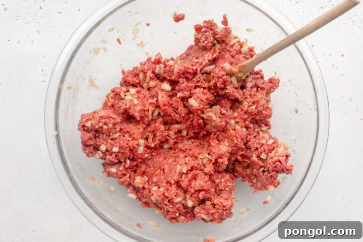 Mixture for Whole30 meatloaf in a large glass mixing bowl with a wooden spoon.