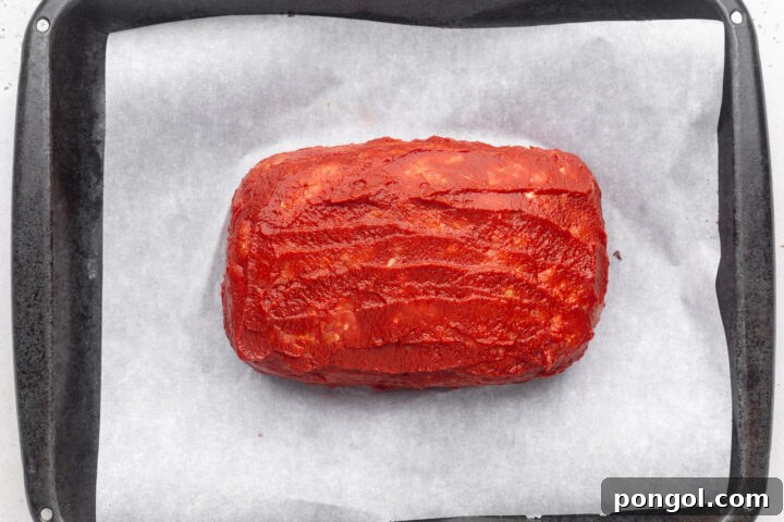 Whole30 meatloaf, before being cooked, coated in a sugar-free tomato glaze on a sheet pan with parchment paper.