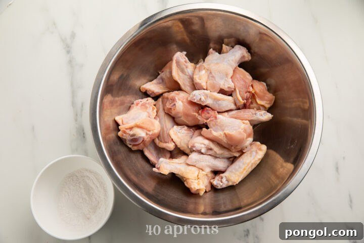 Overhead view of raw chicken wings in a large silver bowl, next to a Whole30 "breading" mixture in a small white bowl.