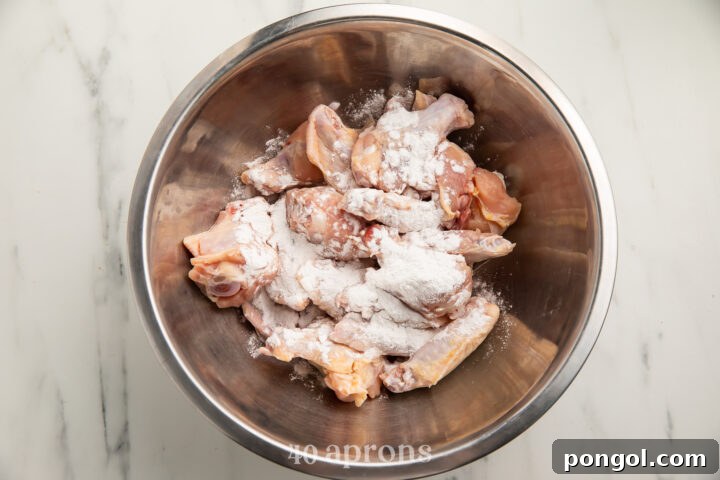 Overhead view of chicken wings topped with a Whole30 "breading" mixture in a large silver mixing bowl.