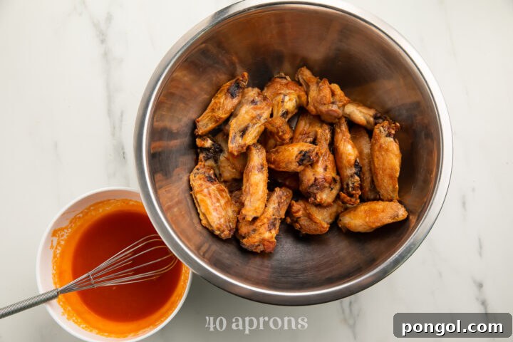 Cooked Whole30 buffalo wings in a large silver mixing bowl, next to Whole30 buffalo sauce in a small white bowl.