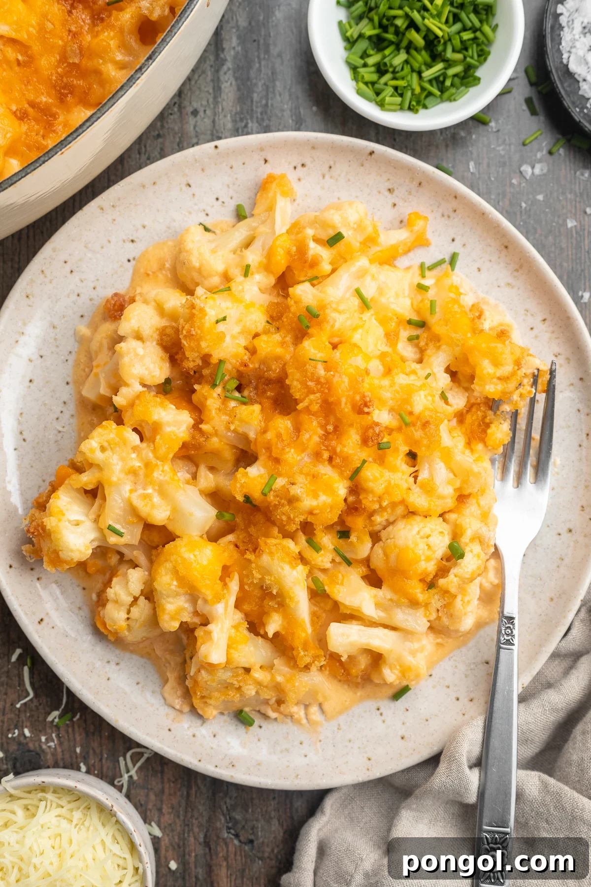 Overhead view of keto mac and cheese plated on a serving plate with a fork on a dark table, highlighting its rich texture and golden topping.