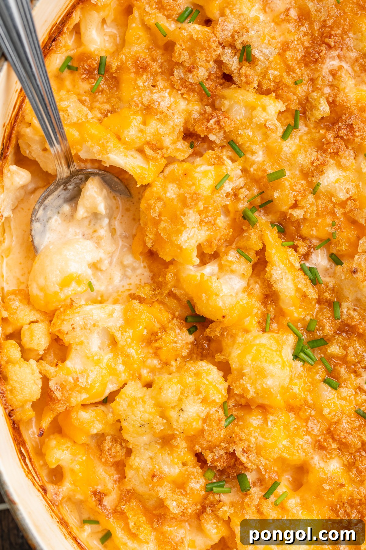 Close-up view of keto mac and cheese in a casserole dish with a large silver spoon, showing the gooey cheese and crispy topping.