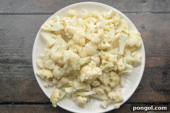 Overhead view of cauliflower florets on a large white round plate, ready for cooking.