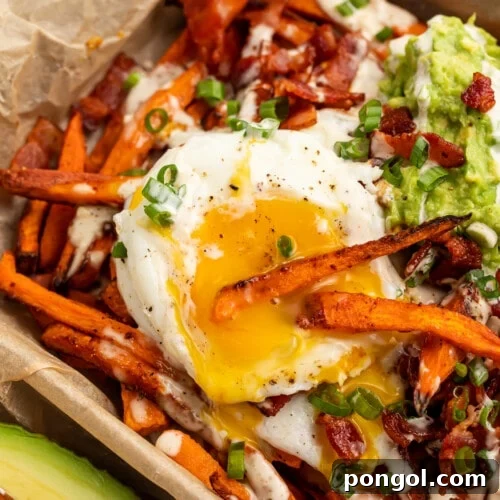 Close-up overhead view of Whole30 Loaded Sweet Potato Fries dipped into a fried egg