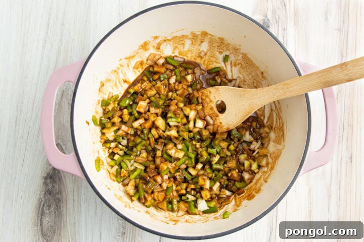 Roux and holy trinity (celery, green bell pepper, and onions) mixed together in a large heavy-bottomed pot with a wooden spoon.