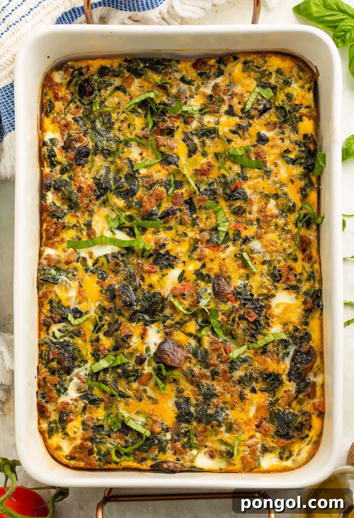 Savory Whole30 Keto Sausage and Egg Breakfast Bake 3 Whole30 breakfast casserole with sausage, eggs, mushrooms, and spinach in a white baking dish, garnished with fresh basil.