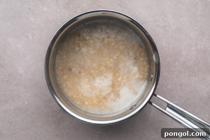 Cooked oatmeal in a silver saucepan with a single handle, showing less water than before.