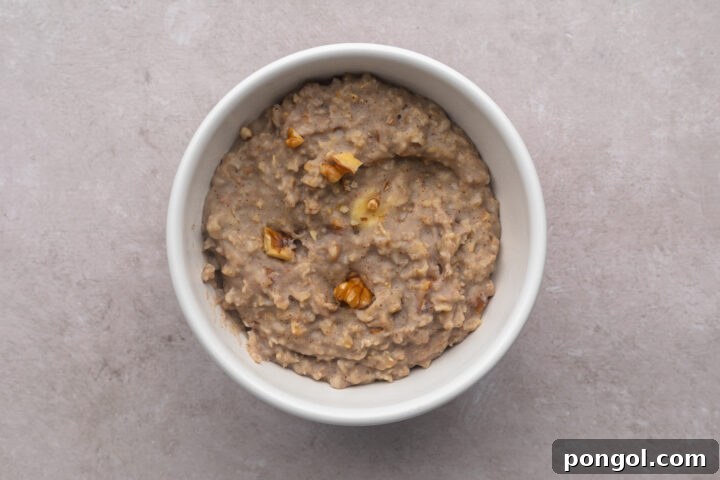 Top-down view of a white bowl filled with banana nut protein oatmeal topped with slivers of chopped walnuts.