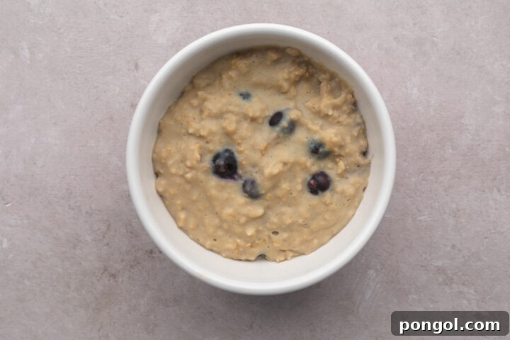 Top-down look at a white bowl filled with blueberry vanilla protein oatmeal on a neutral table.