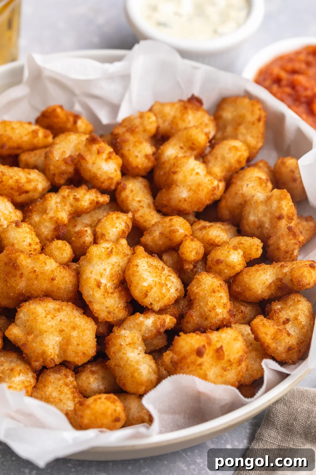Golden Crispy Air Fryer Popcorn Shrimp 2 Overhead, angled photo showing a large white bowl filled with air fryer popcorn shrimp. In the background are ramekins of tartar sauce and ketchup.
