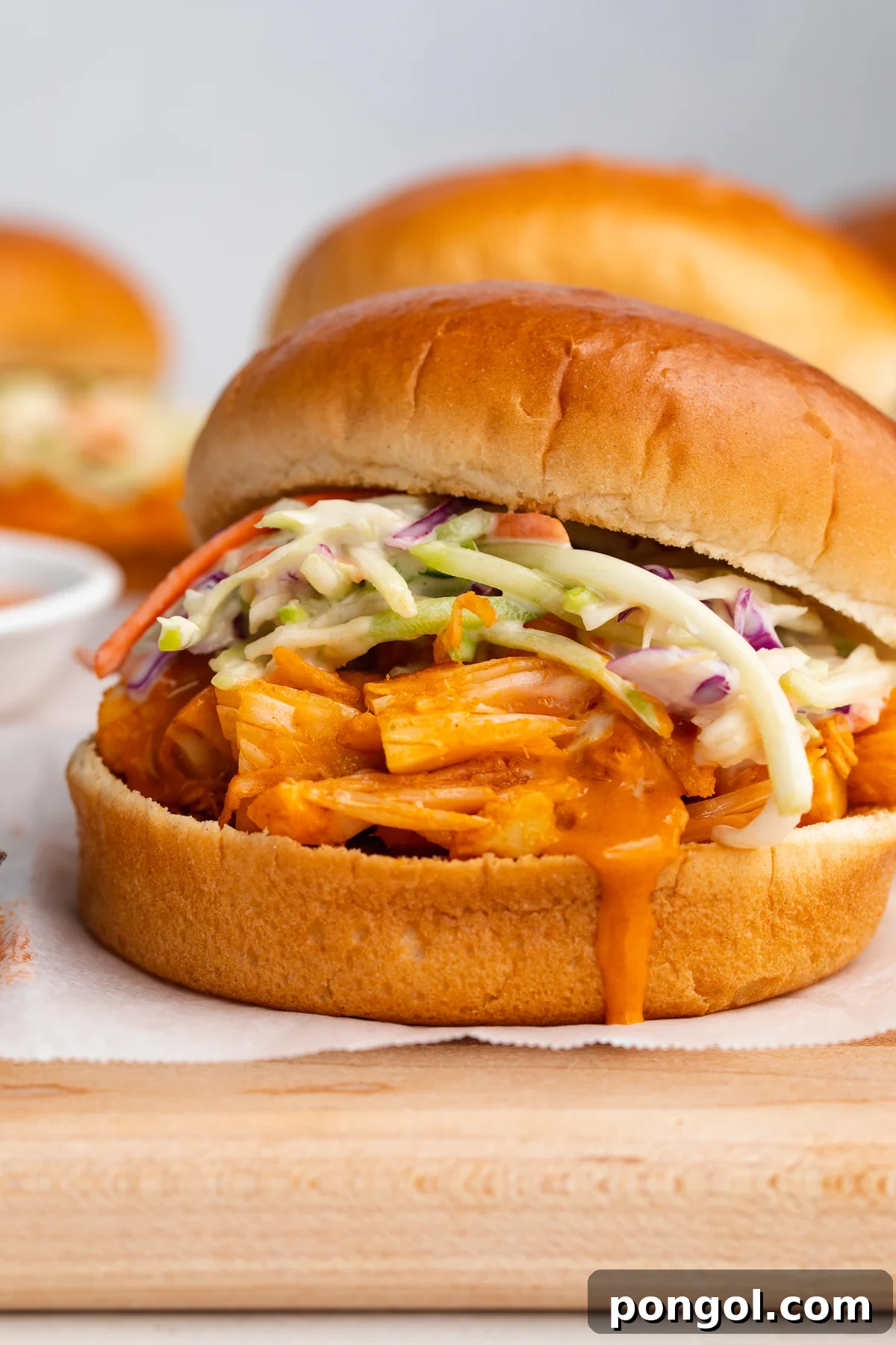 Zingy Buffalo Jackfruit Sandwich 2 Delicious Buffalo jackfruit sandwiches on a rustic wooden cutting board, garnished with fresh cilantro and ready to serve.