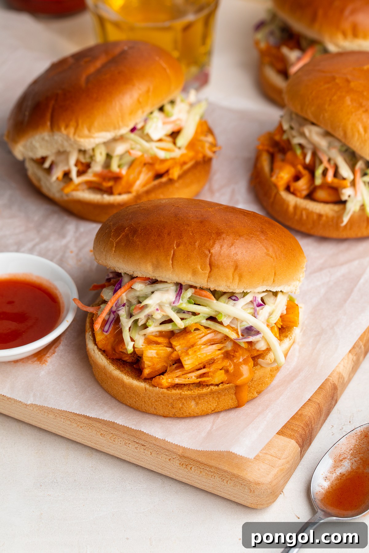 Zingy Buffalo Jackfruit Sandwich 3 An appetizing close-up of three Buffalo jackfruit sandwiches, artfully arranged on a wooden cutting board with parchment paper, highlighting the vibrant colors and textures of the filling and coleslaw.